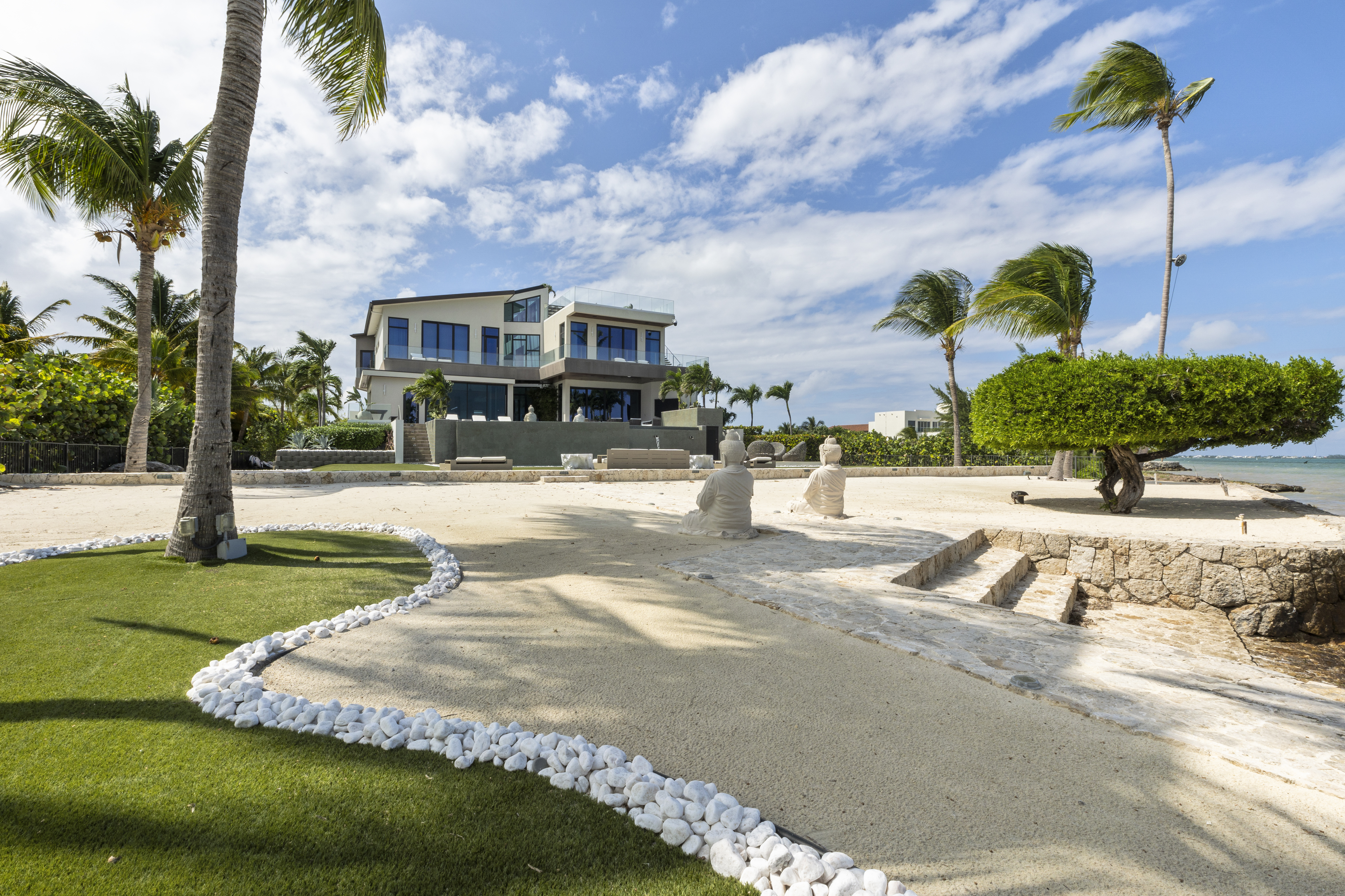 House with sea front view surrounded by trees and long gravel pathway towards entrance